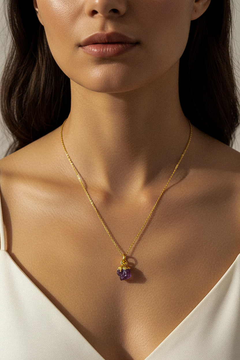 Close-up of a woman wearing a gold necklace with a purple Amethyst pendant.