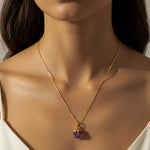 Close-up of a woman wearing a gold necklace with a purple Amethyst pendant.