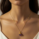 Close-up of a woman wearing a gold necklace with a purple Amethyst pendant.