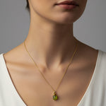 Woman wearing a gold necklace with a green peridot pendant against a neutral background