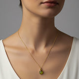 Woman wearing a gold necklace with a green peridot pendant against a neutral background