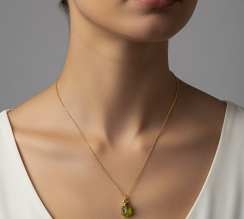 Woman wearing a gold necklace with a green peridot pendant against a neutral background