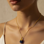 Close-up of a woman wearing a gold necklace with a dark blue Raw Sapphire crystal pendant against a neutral background