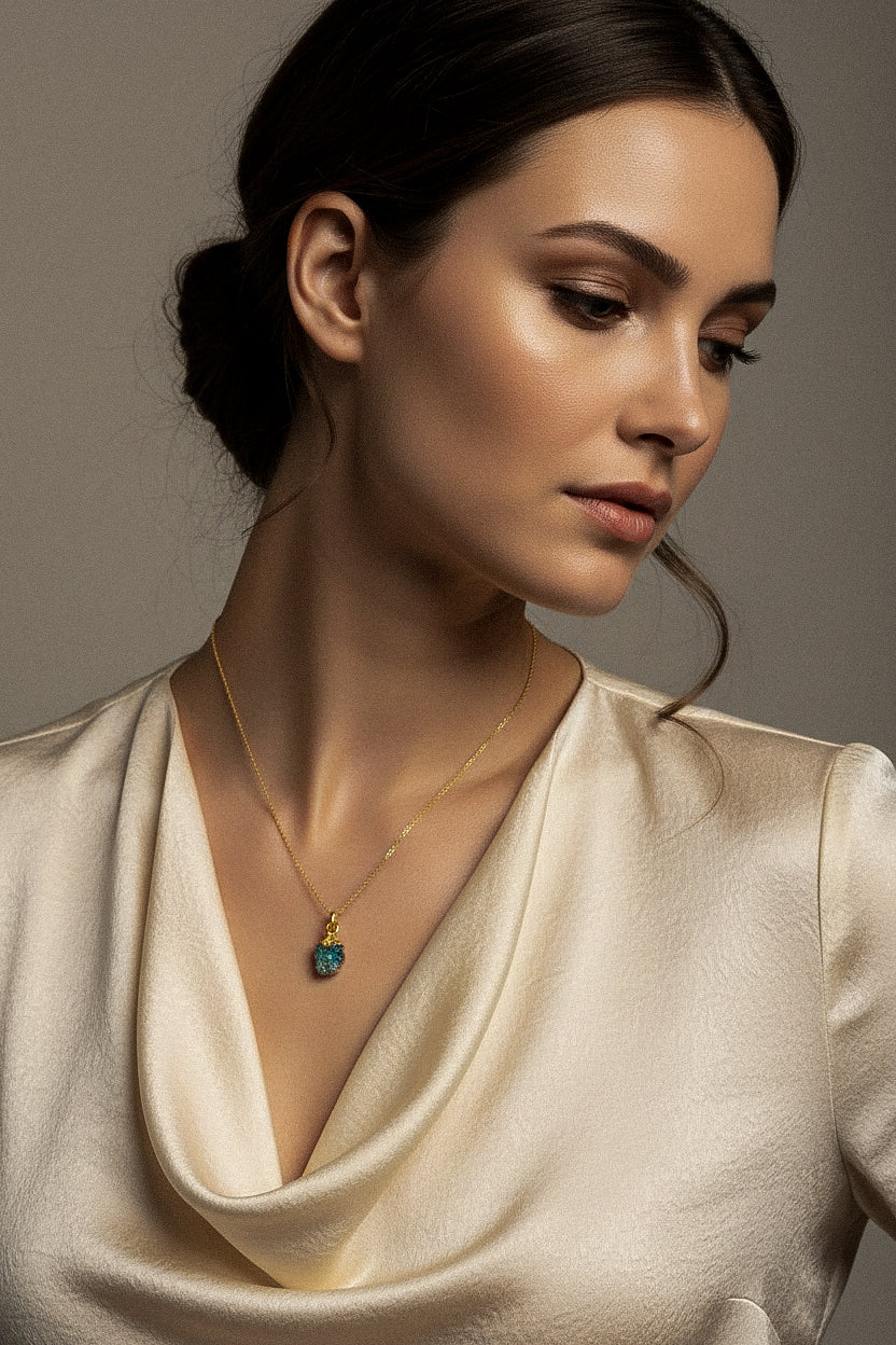 Woman wearing a gold necklace with a raw Turquoise crystal pendant against a neutral background