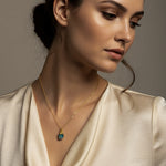Woman wearing a gold necklace with a raw Turquoise crystal pendant against a neutral background