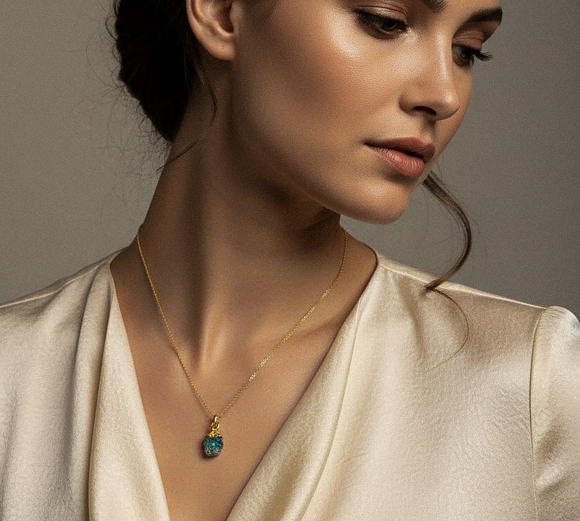 Woman wearing a gold necklace with a raw Turquoise crystal pendant against a neutral background