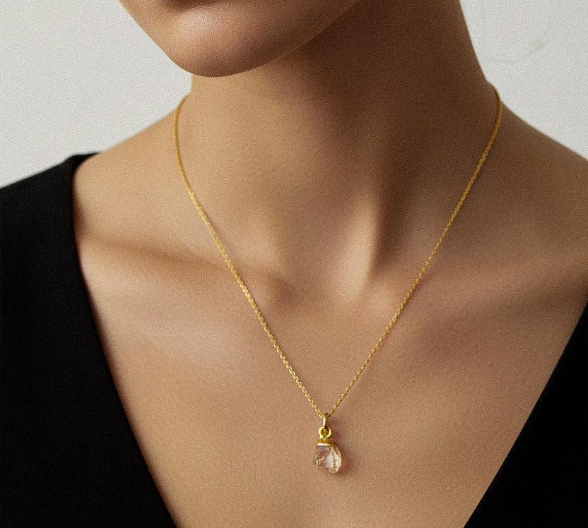 Woman wearing a gold necklace with a raw citrine chakra pendant against a neutral background