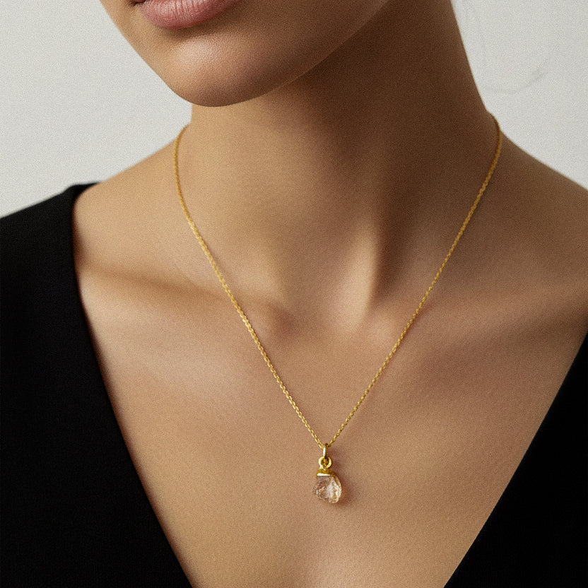 Woman wearing a gold necklace with a raw citrine chakra pendant against a neutral background