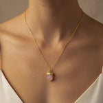 Close-up of a woman wearing a gold necklace with a pink pendant against a neutral background
